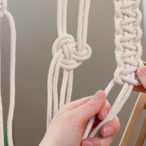 hands tying knots with macramé cord