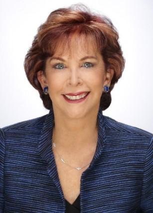 Terry Savage, a Caucasian female with short and curled auburn hair, light blue eyes and sapphire earrings.  She wears red lipstick and a dark blue blazer against a white background.