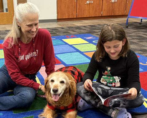 lady in red shirt, red dog, and young girl reading a book