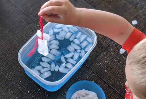 child with container of blue water and ice cubes