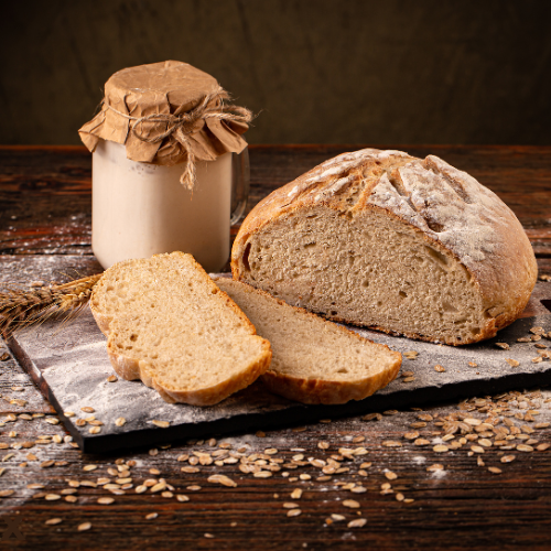 Rustic sourdough sliced on a cutting board with starter in a glass jar. 